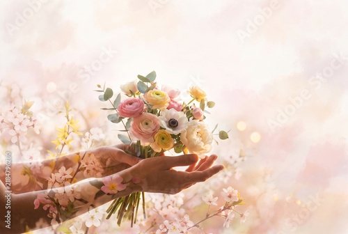 Hands offering bouquet of ranunculus and peonies among cherry blossom branches