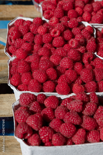 Foto Fresh organic red raspberries Rubus idaeus filled in paper baskets on wooden display at outdoor local farmers market, close-up vertical high angle view