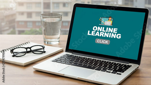 Laptop displaying online learning portal with a glass of water and notebook on a wooden desk during daytime
