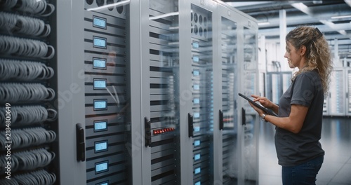 Female Data Center Engineer Uses Tablet to Inspect Server Rack Indicators and Patch Cable Routing, Performing Mobile Equipment Inventory and Physical Infrastructure Audit During on site Maintenance.