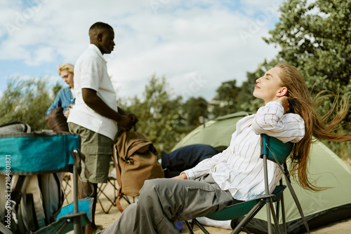 Canvas Print Young Caucasian woman relaxing in chair at campsite with African American young adult friend nearby