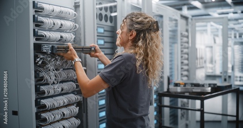 Female Engineer Mounts Replacement Network Switch in Modern Data Center Rack, Performing Hardware Upgrade and Infrastructure Maintenance to Improve Network Reliability and Support Business Operations.