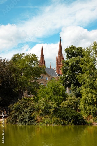 фотографія Wiesbaden, Hesse, Germany – Marktkirche church towers rising above lush greenery and pond in scenic urban park landscape