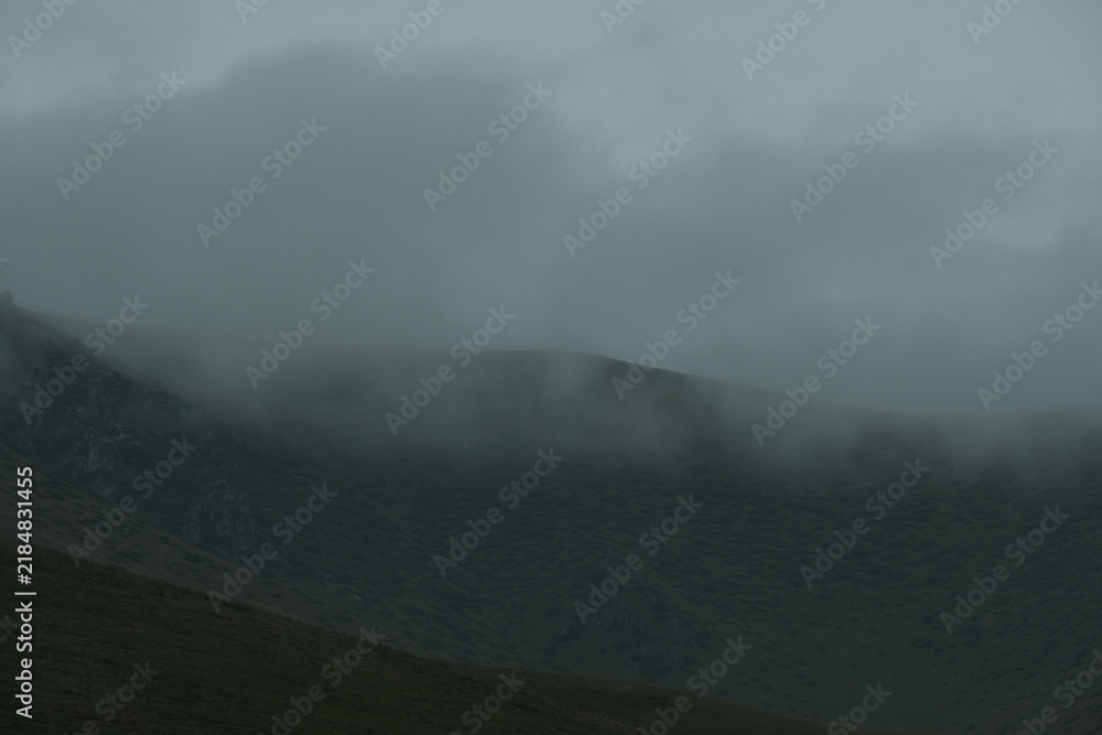 Obraz premium A dark, moody mountain landscape covered in thick fog and low clouds. This minimalist, atmospheric image 