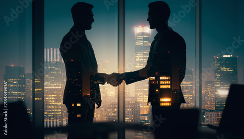Double Exposure Silhouette of Businessmen Shaking Hands Over Night City Skyline