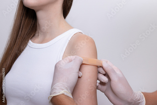 Doctor, nurse applying adhesive bandage to woman's upper arm after completing vaccine injection. Concept of HPV vaccination, influenza immunization, cervical cancer prevention, adult vaccination.