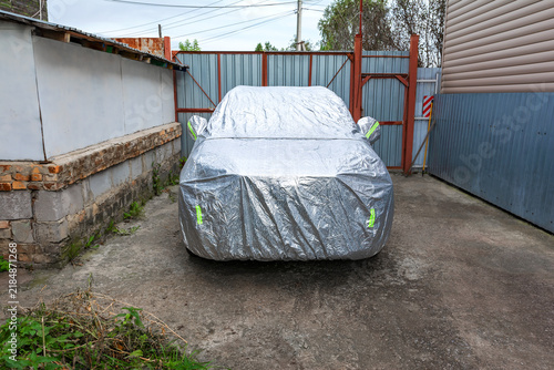 A passenger car is parked under a silver protective covering in the courtyard of a private residence.