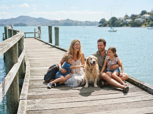 Family of four and a golden retriever seated on a wooden lakeside pier