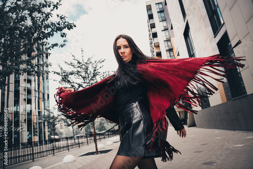 Fotografie Confident young woman in stylish urban setting wearing red shawl and leather ski