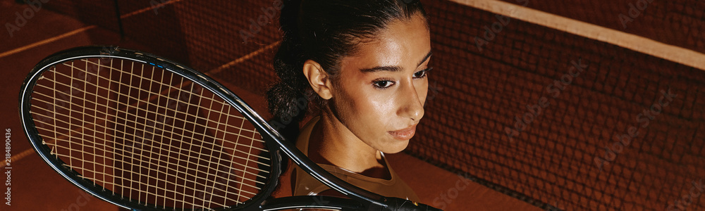 Fototapeta premium Young adult multiethnic woman holding tennis racket on court, focused during training match. Visual concept for fitness campaigns and sports marketing, high angle view