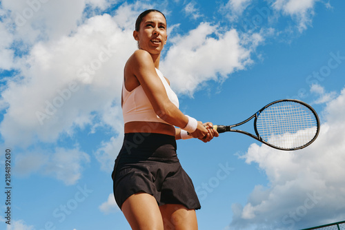 Принти на полотні Multiethnic young adult woman holding racket ready to hit backhand during tennis match