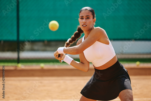 Fotografie Young adult woman hitting ball during tennis match on outdoor clay court