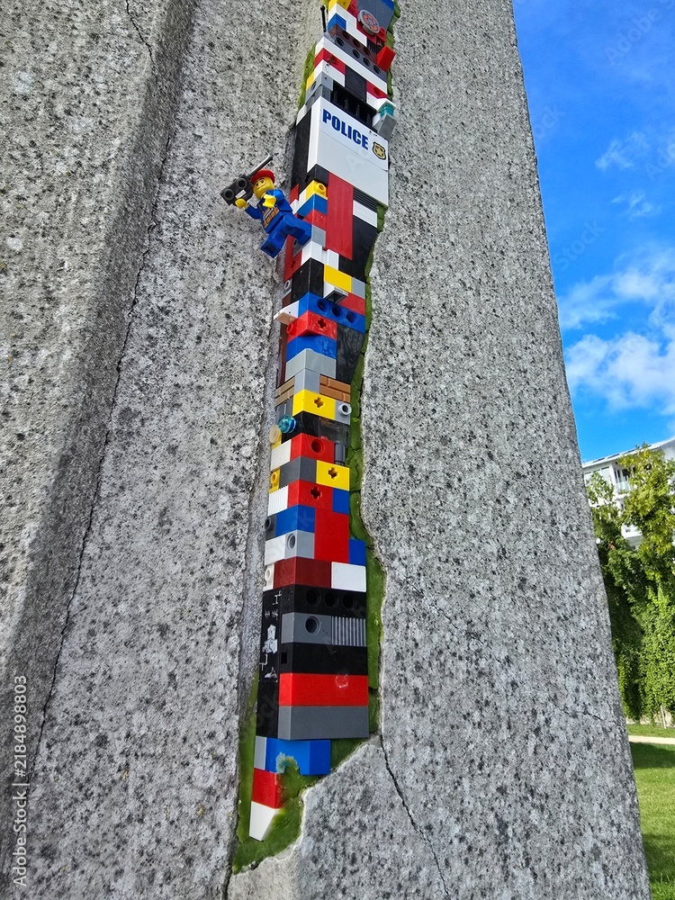 Fototapeta premium Lego dispatchwork street art in a cracked stone wall with police brick and climbing minifigure Sassnitz Ruegen Germany September 06 2025