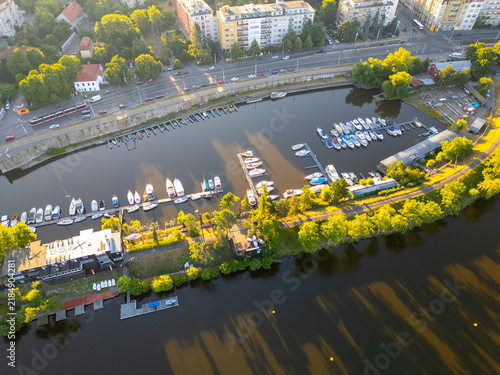 Aerial view of Cesky Yacht Klub marina on the Vltava river with docked boats, lush green trees, and urban surroundings in Prague, Prague, Czechia.