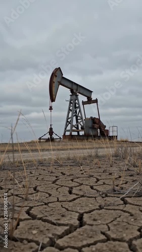 Oil pumpjack in drought cracked field under cloudy sky