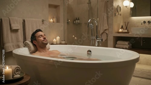 Relaxed man bathing in luxury tub surrounded by lit candles in serene spa bathroom. Warm ambient lighting, peaceful mood, wellness lifestyle.