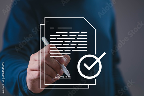 Fotografie Business document signing concept showing a professional signing paperwork with a pen, approval checkmark, and signature, agreement, authorization, verification, compliance, and official approval