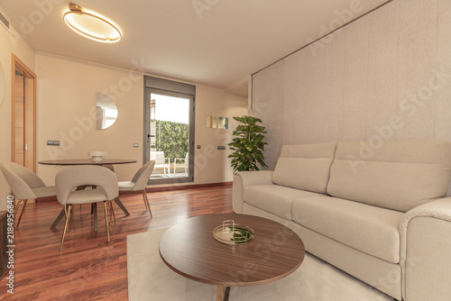 Cozy living room with a beige upholstered sofa, round wooden coffee table, and terrace access through glass doors.