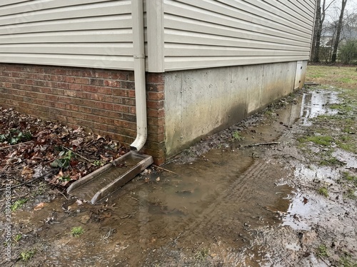 flood risk Corner of a house with water pooling from a downspout onto wet ground.