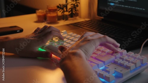 Close-up of hands typing quickly on an illuminated RGB mechanical keyboard in a dimly lit home office workspace at night.