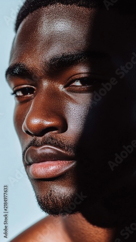 Close-up portrait showcasing rich dark skin texture and defined facial features against light background, highlighting natural beauty and strength in contemporary beauty photography