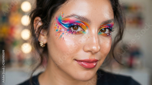 Person showcasing intricate face art with blue and rainbow swirls around their eyes.