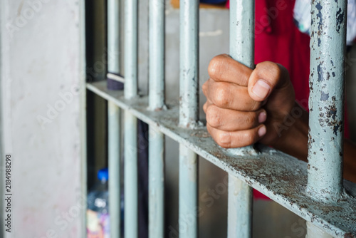 Obraz na plátně Close up view of hands behind bars in a prison cell, symbolizing incarceration and the criminal justice system