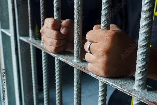 Obraz na plátně Close up view of hands behind bars in a prison cell, symbolizing incarceration and the criminal justice system