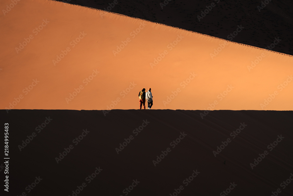 Fototapeta premium Two hikers dwarfed by the slope of a giant dune