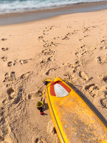 Yellow fish surfboard lying on sandy beach by ocean waves