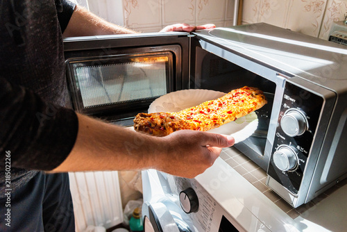 Hands putting a frozen vegetarian baguette pizza into a microwave oven.