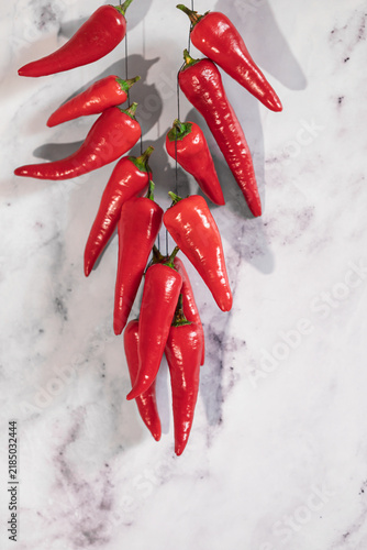 Red chili peppers hanging on light marble with hard shadows