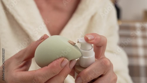 Close-up of a woman in a bathrobe applying foundation or makeup base to a sponge for application to her face. Makeup and cosmetics concept.