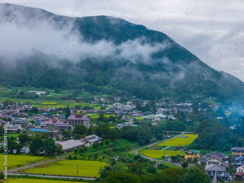 Low cloud on mountain over small village by green rice fields