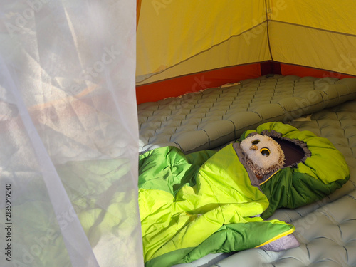 Cute owl plush toy resting inside a green sleeping bag in a tent