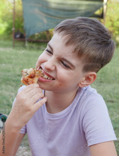 Young boy smiles while eating a crispy, savory snack outdoors