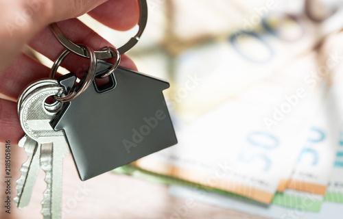 Hand holding house keys with money background