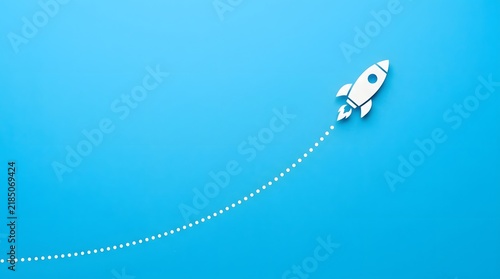 White paper cut style rocket with fins and flame detail flying upward on a diagonal path marked by a dotted line against a plain blue surface