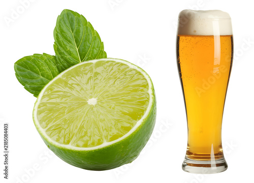 Fresh lime wedge and mint leaves beside a glass of golden beer with frothy head isolated on transparent background