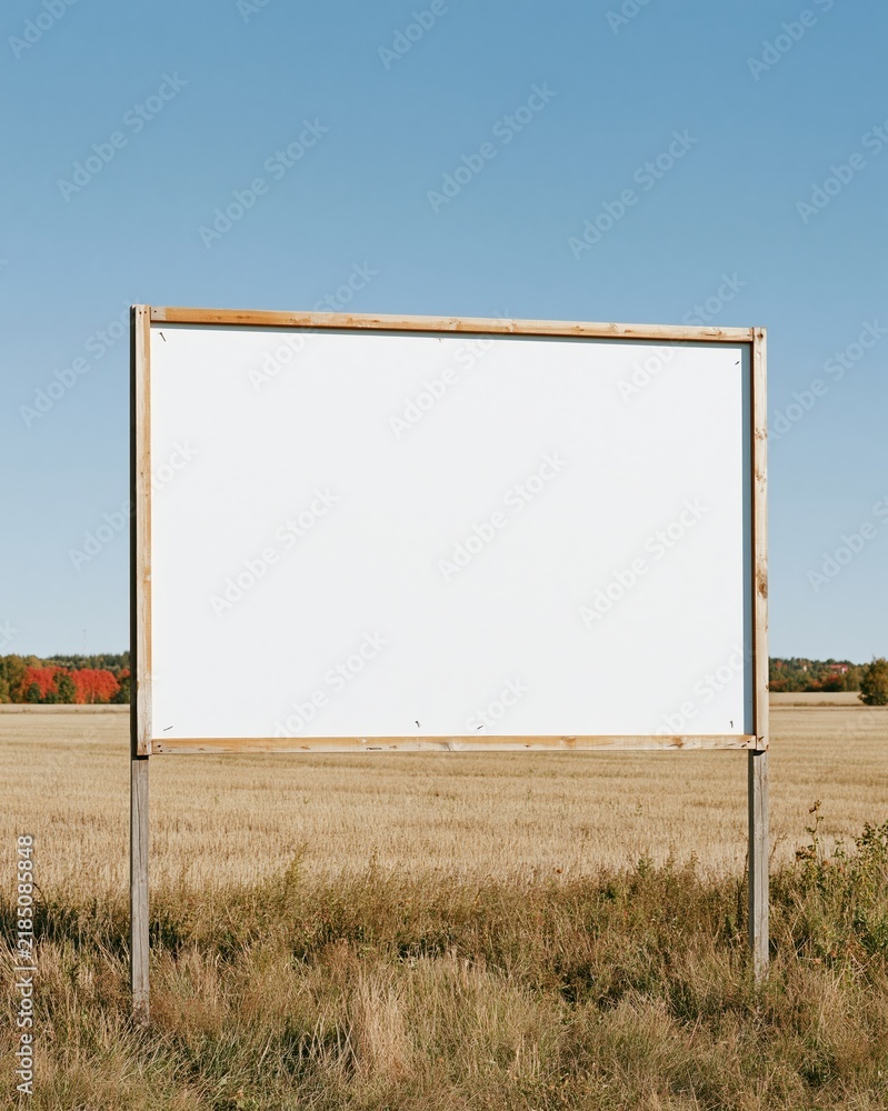 Obraz premium Blank rectangular sign in a weathered wooden frame standing in a rural field, featuring a matte white surface for mockup and copy space