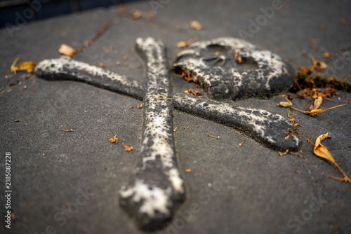 Konstfotografi Selective focus close-up of carved stone skull and crossbones memento mori symbol on weathered tombstone