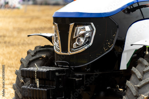 фотографія Close-up of modern autonomous electric tractor front end with LED headlights and ballast weights on field