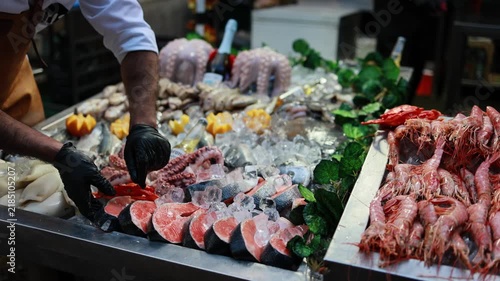 Fishmonger Arranging Fresh Salmon Steaks and Seafood on Ice at Market Display