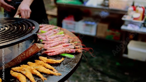 Seafood grilling on round charcoal grill at street food market. Fried fish and fresh prawns cooking with smoke. Man cooking asian street food, street food festival concept