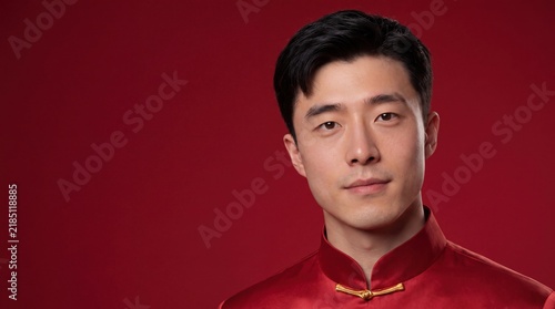 Young Asian man in traditional red shirt against crimson background