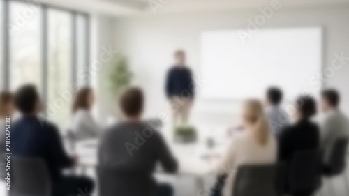 Presenter addressing seated colleagues beside a bright screen wall, Full Gaussian Blur Abstract