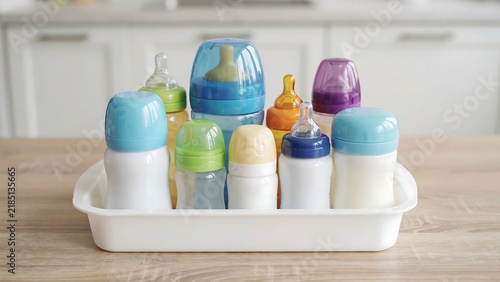 Assorted colorful baby bottles organized in a storage tray on kitchen counter