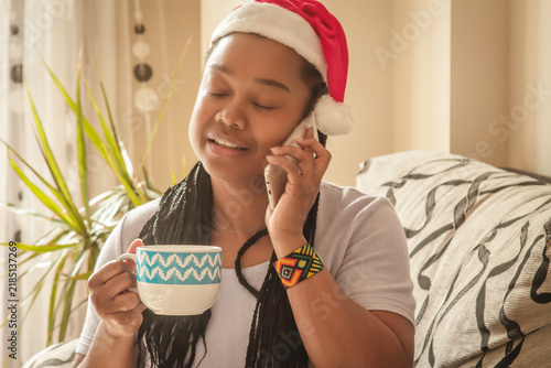Relaxed black woman with a hot drink in her hands and a mobile phone enjoying the Christmas holidays