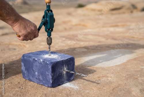 Obraz na płótnie Hand Drill Bores Blue Block on Stone Surface