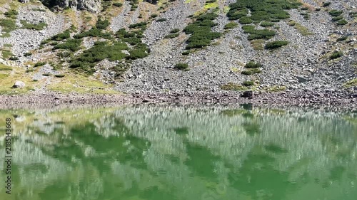 Panning shot of the emerald glacial Lake Mija and rocky alpine slope in Parang Mountains, Romania. Nature and travel video, 4K, 60fps.